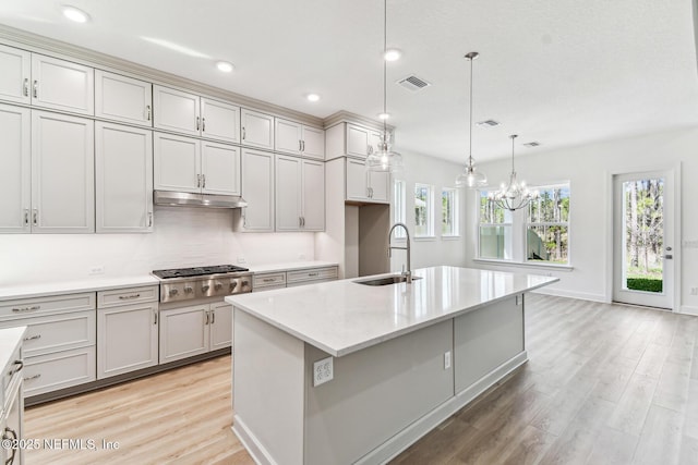 kitchen with visible vents, stainless steel gas cooktop, under cabinet range hood, light wood-type flooring, and a sink