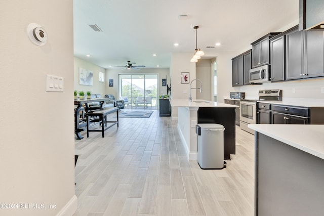 kitchen featuring sink, light hardwood / wood-style flooring, pendant lighting, stainless steel appliances, and a kitchen island with sink