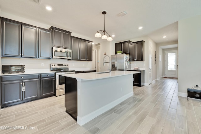 kitchen featuring sink, stainless steel appliances, dark brown cabinetry, an island with sink, and decorative light fixtures