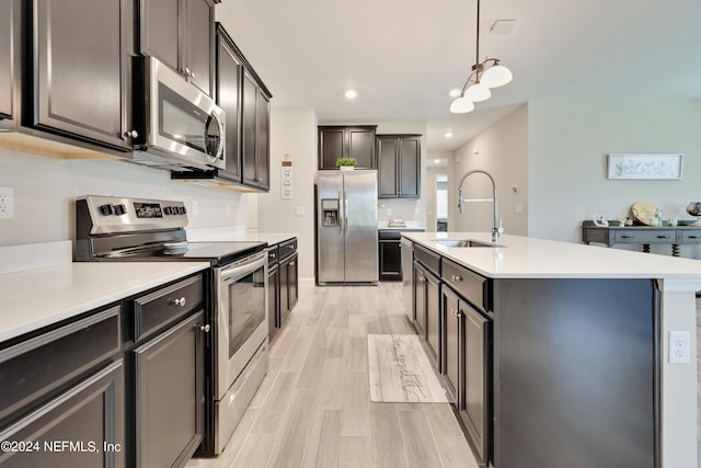 kitchen with sink, a center island with sink, pendant lighting, stainless steel appliances, and light hardwood / wood-style floors