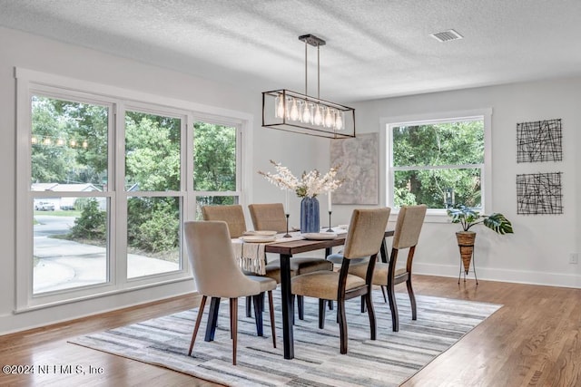 dining area with a textured ceiling, light wood-type flooring, and a chandelier