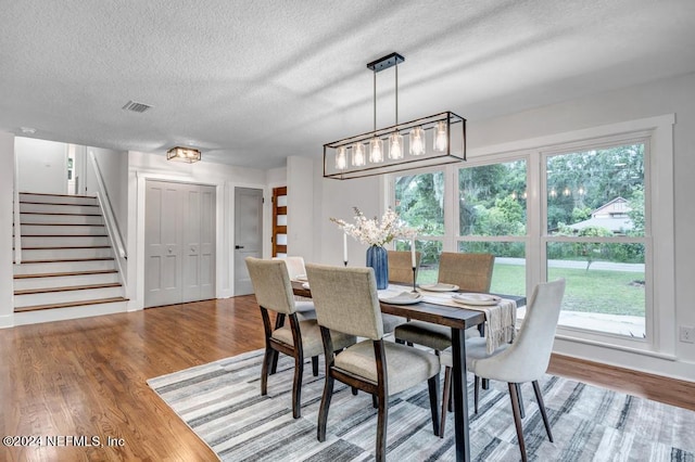 dining area featuring a textured ceiling, a healthy amount of sunlight, an inviting chandelier, and wood-type flooring