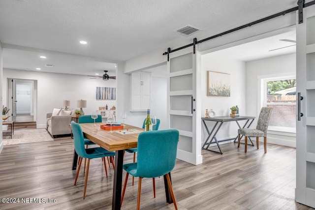 dining area featuring a barn door, ceiling fan, light wood-type flooring, and a textured ceiling