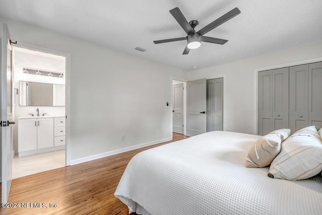 bedroom with ensuite bath, sink, ceiling fan, two closets, and light hardwood / wood-style floors