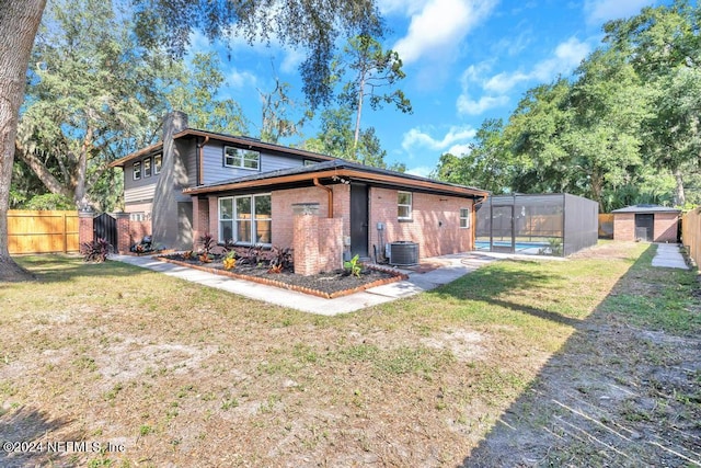 back of house with a storage shed, central AC unit, a lawn, and a pool