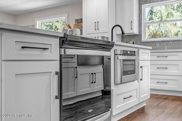 kitchen with oven, white cabinetry, hardwood / wood-style floors, and sink