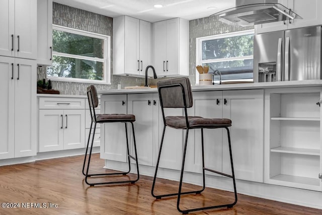 kitchen with stainless steel fridge, white cabinetry, extractor fan, and light hardwood / wood-style floors