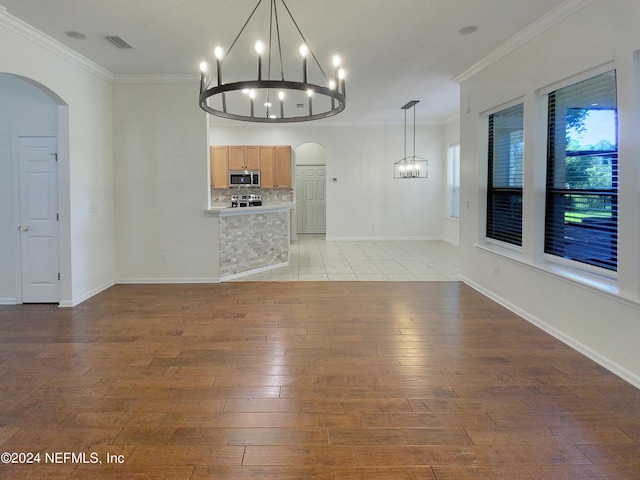 unfurnished living room featuring ornamental molding, an inviting chandelier, and light hardwood / wood-style flooring