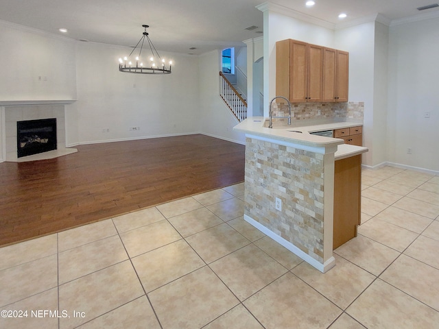 kitchen featuring hanging light fixtures, ornamental molding, light hardwood / wood-style flooring, a tiled fireplace, and backsplash