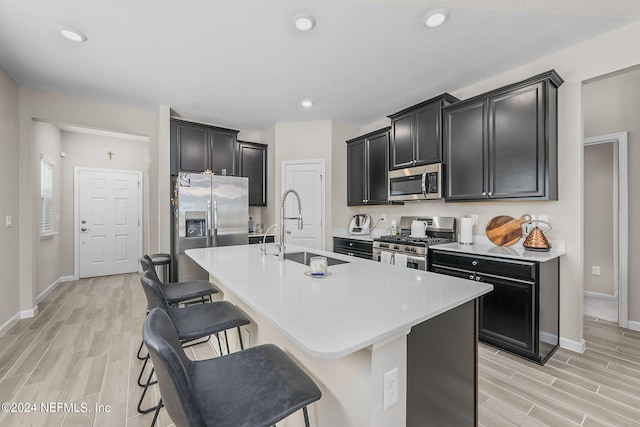 kitchen with appliances with stainless steel finishes, sink, light wood-type flooring, a breakfast bar area, and a kitchen island with sink