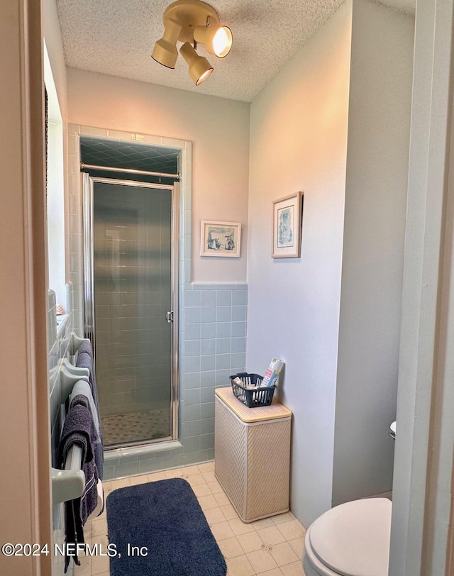 bathroom featuring toilet, a textured ceiling, tile walls, tile patterned flooring, and a shower with door