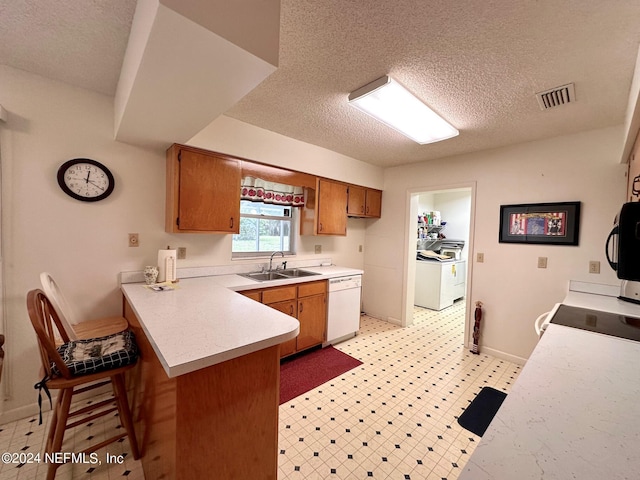 kitchen with kitchen peninsula, white dishwasher, sink, a kitchen bar, and a textured ceiling