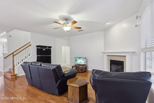 living area with ceiling fan, a tile fireplace, wood finished floors, visible vents, and stairs