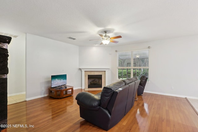 living room with baseboards, a textured ceiling, a tiled fireplace, and wood finished floors