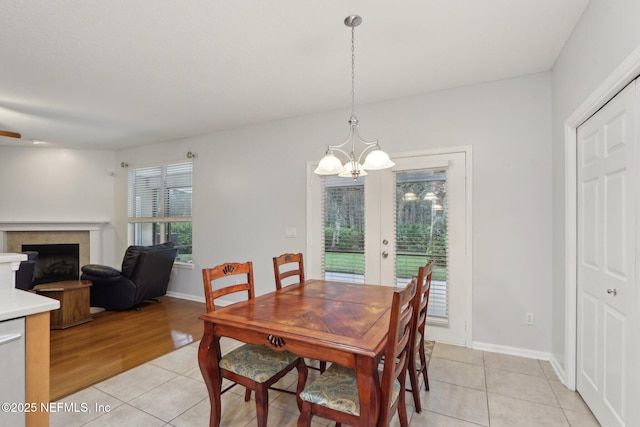 dining area with light tile patterned floors, a fireplace, baseboards, and a notable chandelier