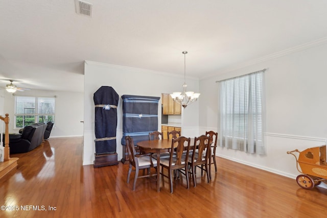 dining space featuring ceiling fan with notable chandelier, wood finished floors, visible vents, baseboards, and ornamental molding