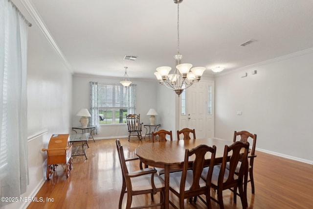 dining space featuring baseboards, wood finished floors, visible vents, and crown molding