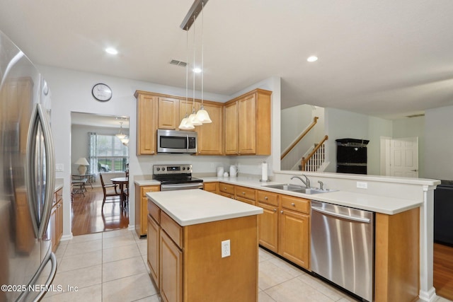 kitchen with appliances with stainless steel finishes, decorative light fixtures, a peninsula, light countertops, and a sink