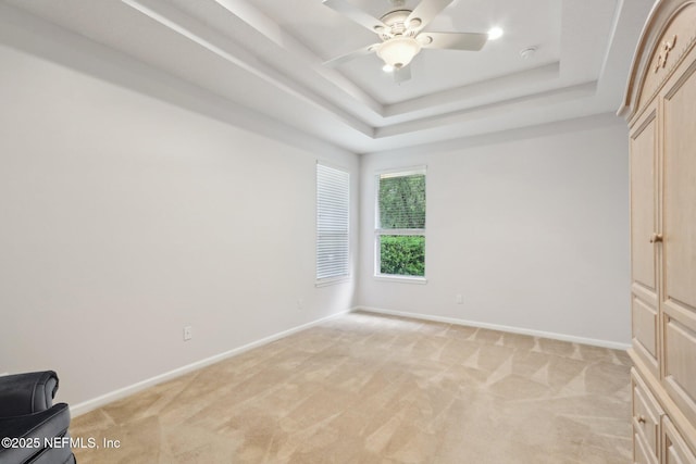 unfurnished bedroom with baseboards, a tray ceiling, a ceiling fan, and light colored carpet