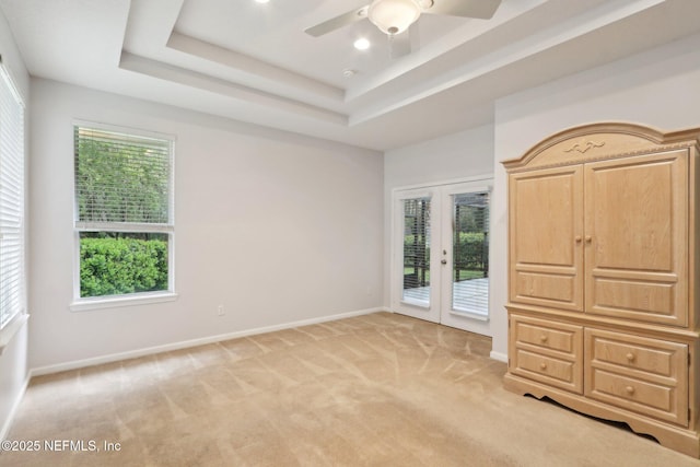 unfurnished bedroom with light carpet, baseboards, a raised ceiling, access to exterior, and french doors