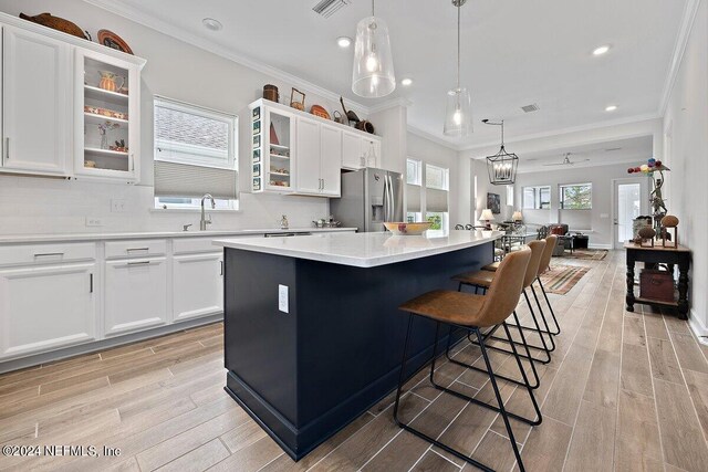 kitchen with tasteful backsplash, stainless steel fridge, pendant lighting, light wood-type flooring, and a center island