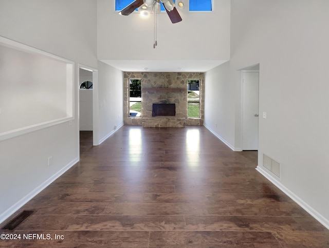 unfurnished living room featuring dark hardwood / wood-style flooring, a towering ceiling, ceiling fan, and a fireplace