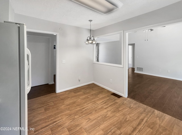 unfurnished dining area with hardwood / wood-style floors, a notable chandelier, and a textured ceiling