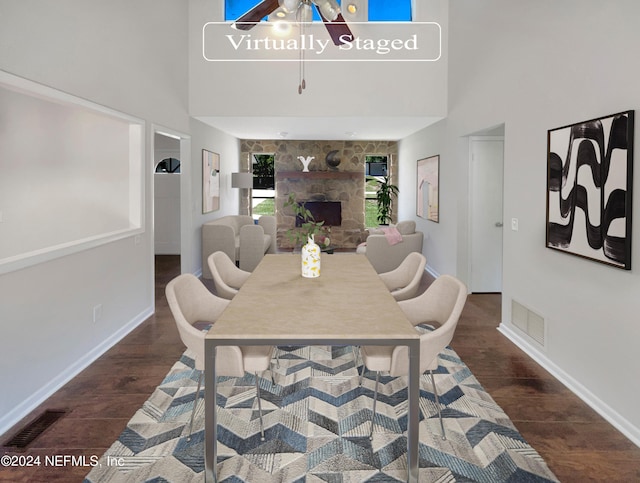 dining space with a stone fireplace, dark hardwood / wood-style floors, and a high ceiling