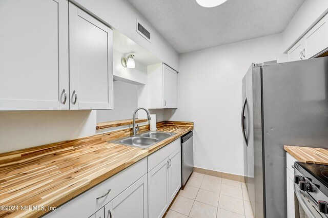 kitchen with stainless steel appliances, sink, light tile patterned floors, and white cabinetry