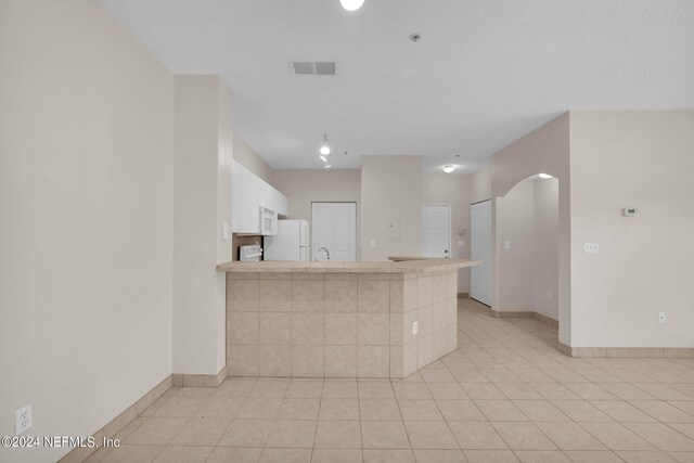 kitchen with kitchen peninsula, white appliances, light tile patterned floors, and white cabinets