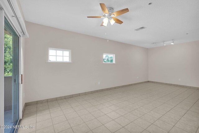 tiled spare room with ceiling fan, track lighting, and a wealth of natural light