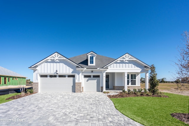 view of front of house featuring a garage, brick siding, decorative driveway, board and batten siding, and a front yard