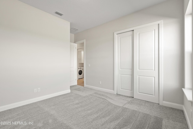 unfurnished bedroom featuring washer / clothes dryer, a closet, and light carpet