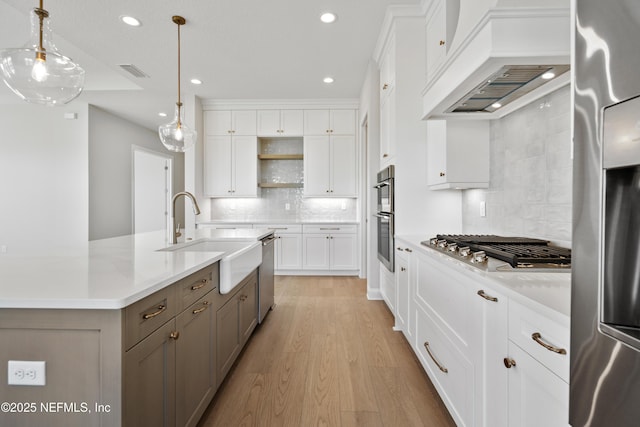 kitchen with custom exhaust hood, appliances with stainless steel finishes, white cabinets, decorative light fixtures, and sink