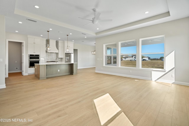 unfurnished living room with ceiling fan, a tray ceiling, light hardwood / wood-style floors, and sink