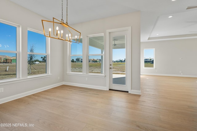 unfurnished dining area with ceiling fan with notable chandelier and light wood-type flooring