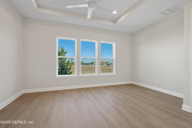 unfurnished room with a raised ceiling, light wood-type flooring, and ceiling fan