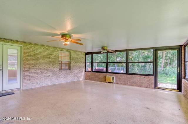 unfurnished sunroom featuring ceiling fan, a wall unit AC, and a healthy amount of sunlight