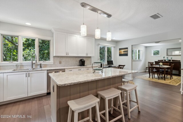 kitchen featuring light stone counters, stainless steel dishwasher, sink, white cabinets, and a center island