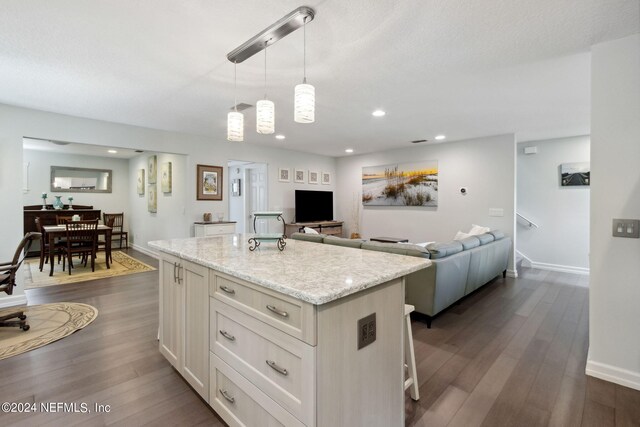 kitchen featuring a center island, hanging light fixtures, a kitchen breakfast bar, light stone counters, and dark hardwood / wood-style floors