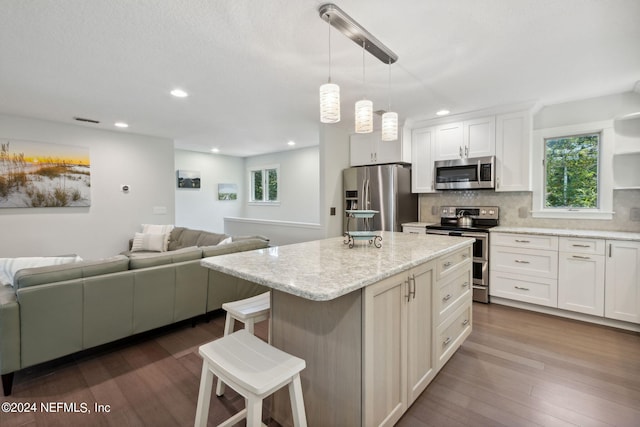 kitchen featuring appliances with stainless steel finishes, a kitchen breakfast bar, decorative light fixtures, white cabinets, and a center island