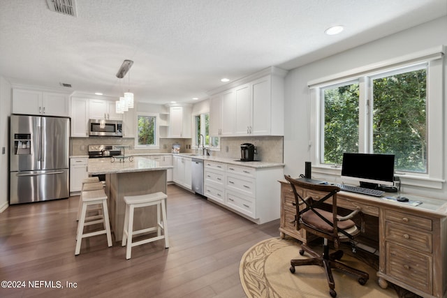 kitchen featuring hanging light fixtures, a center island, sink, appliances with stainless steel finishes, and white cabinets