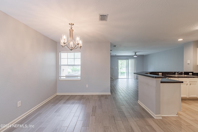 kitchen with ceiling fan with notable chandelier, light hardwood / wood-style flooring, pendant lighting, sink, and white cabinets