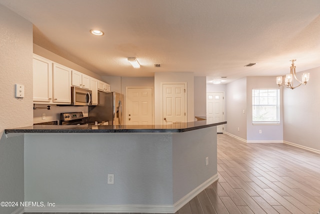 kitchen featuring an inviting chandelier, stainless steel appliances, kitchen peninsula, hardwood / wood-style flooring, and white cabinetry