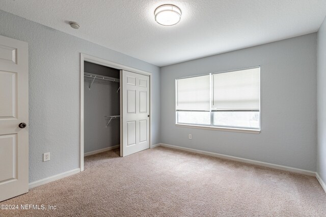 unfurnished bedroom featuring a closet, light carpet, and a textured ceiling