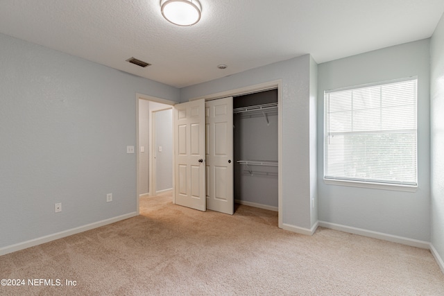 unfurnished bedroom featuring a closet, light colored carpet, and a textured ceiling