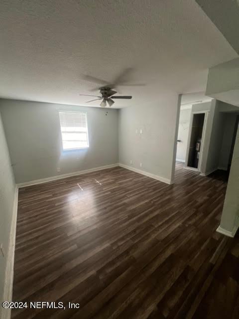 empty room featuring dark wood-type flooring, a textured ceiling, baseboards, and a ceiling fan