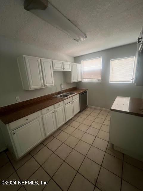 kitchen featuring light tile patterned floors, a textured ceiling, a sink, white cabinetry, and dishwasher