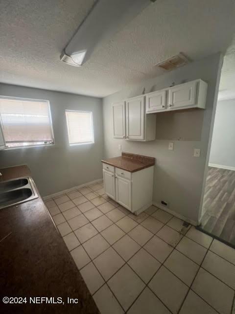 kitchen featuring white cabinets, light tile patterned flooring, a sink, and a textured ceiling