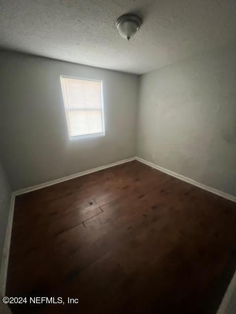 empty room featuring baseboards, dark wood finished floors, and a textured ceiling